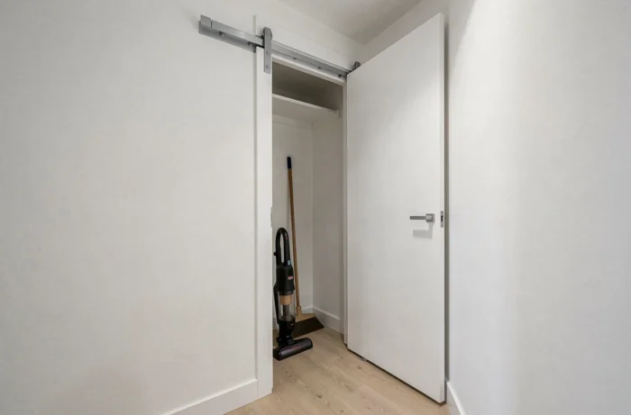 Placard à balais avec porte coulissante mince dans un couloir étroit contenant un aspirateur balai rangé verticalement